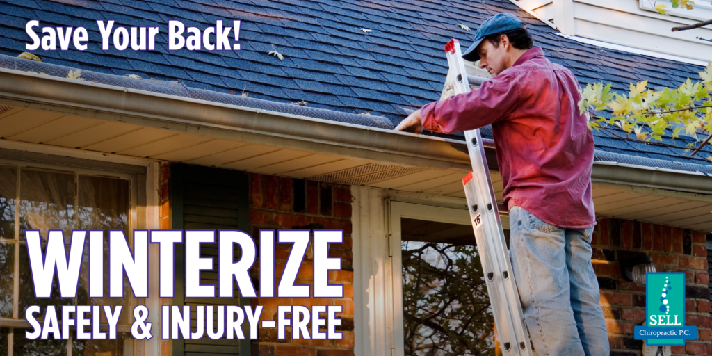 Person wearing jeans and a red plaid shirt stands on a ladder, reaching into a rain gutter with one hand to remove fallen leaves